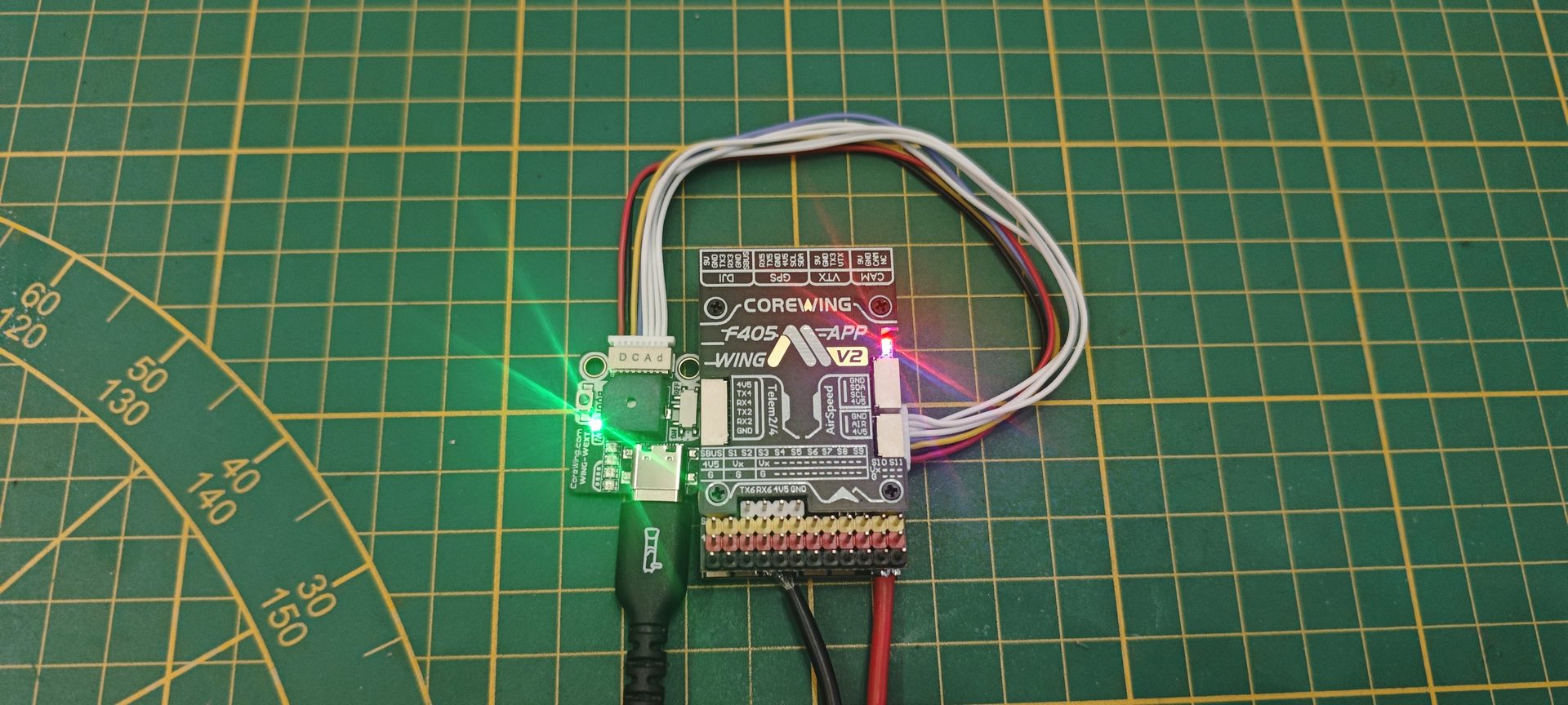 Zbliżenie płytki kontrolera Corewing F405 WING V2 z aktywnymi diodami LED i opisem portów DJI, GPS, VTX, CAM, Telem2/4